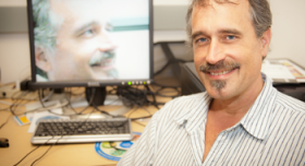 A man smiling in front of a computer screen.