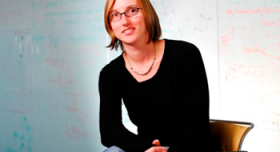 A woman in glasses sitting on a chair in front of a whiteboard.