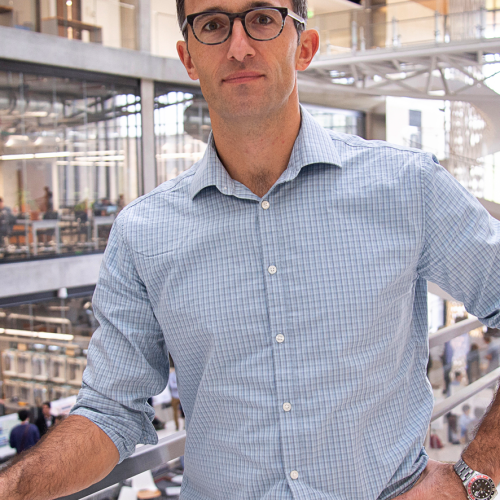 A man in glasses standing on a railing in an atrium.