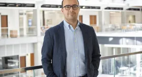 A man in glasses standing on a railing in an office building.