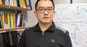 A man in glasses standing in front of a whiteboard.