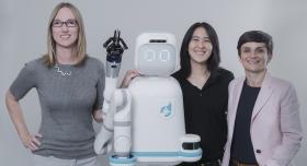 Three women standing next to a robot.