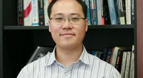 A man in glasses standing in front of a bookshelf.