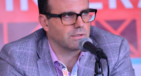 A man in glasses is speaking into a microphone.