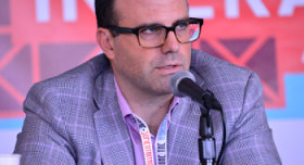 A man in glasses is speaking into a microphone.