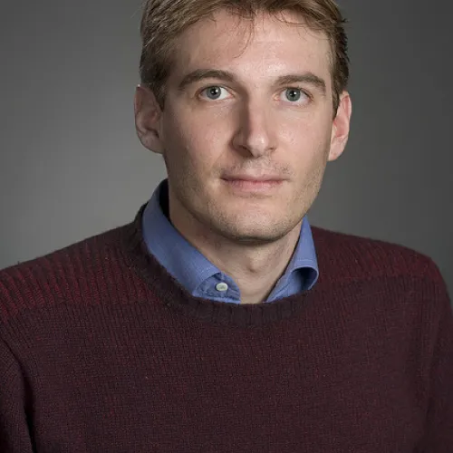 A man in a maroon sweater is posing for a photo.